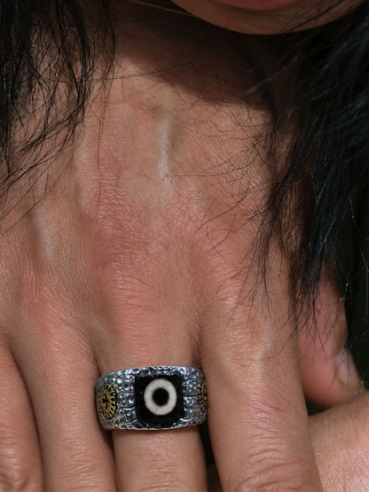 A close-up of a silver-toned ring with a black evil eye design on the center finger of a person's hand.