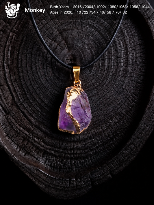 A raw purple amethyst crystal pendant necklace with gold foil accents and a gold bail, displayed on a dark wood slice background. The image includes a 'Monkey' birth chart overlay in the top left corner.