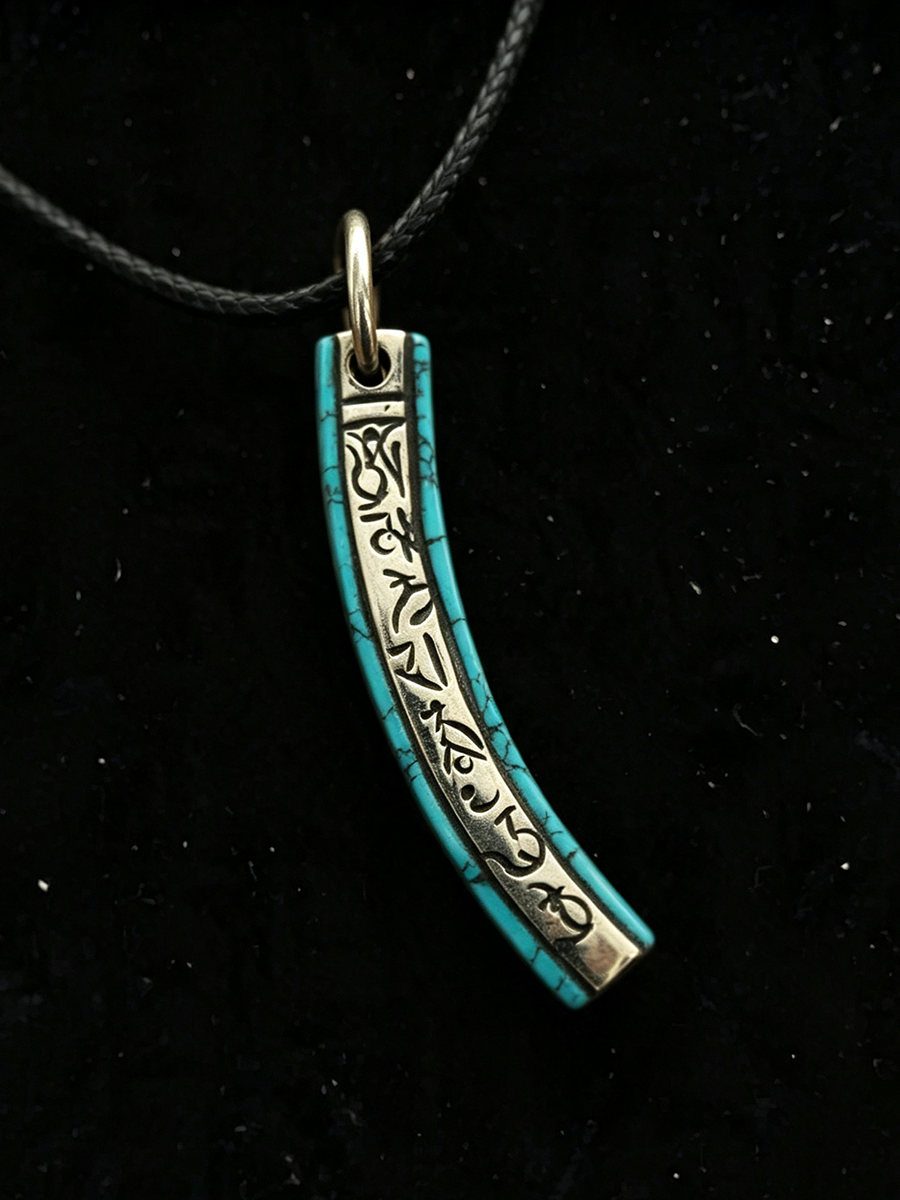 A turquoise and silver crescent-shaped pendant necklace with engraved script, hanging from a black cord against a black background.