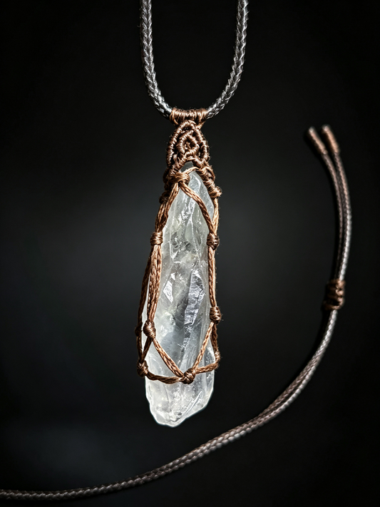 A raw clear quartz crystal pendant necklace wrapped in copper wire, suspended from a silver-toned chain against a dark black background.