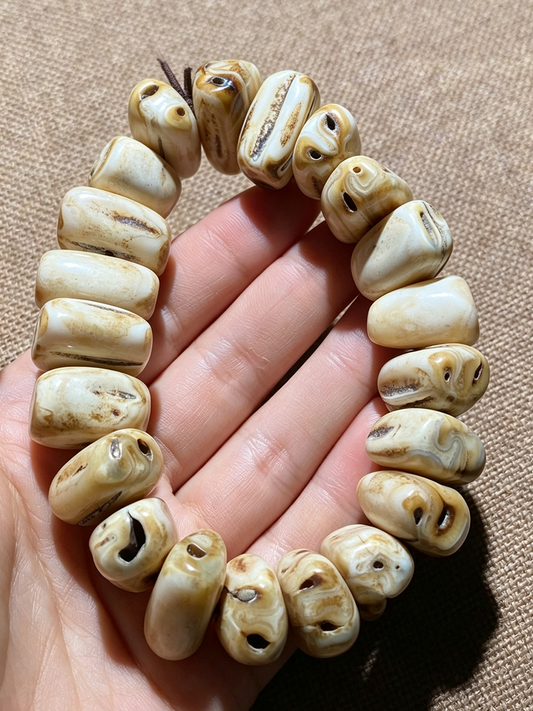 A beaded bracelet made of carved animal skull beads, held in a hand against a textured tan fabric background.