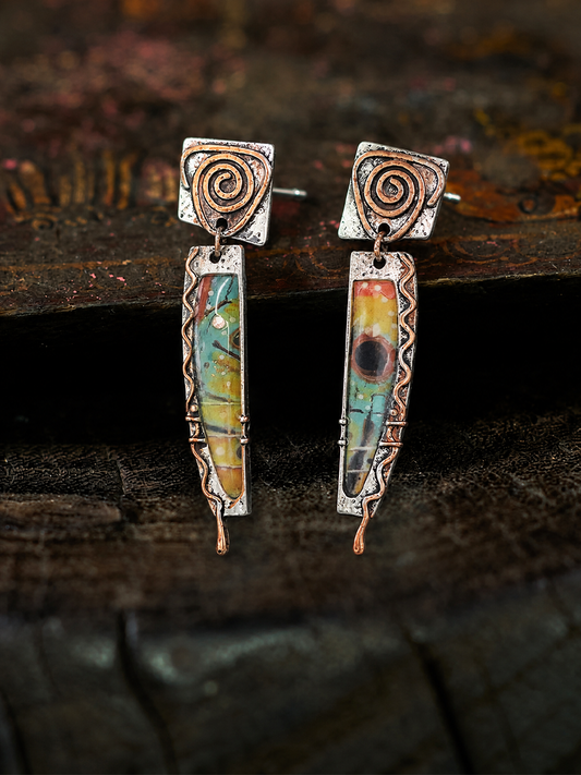 A pair of handmade dangle earrings with silver-toned metal frames, copper-toned spiral details, and colorful marbled resin inserts, displayed on a dark rustic wooden surface.