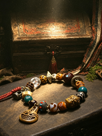 A beaded necklace with a skull pendant and various decorative beads, displayed on a dark wooden surface with a gothic-themed background featuring a chest and draped fabric.