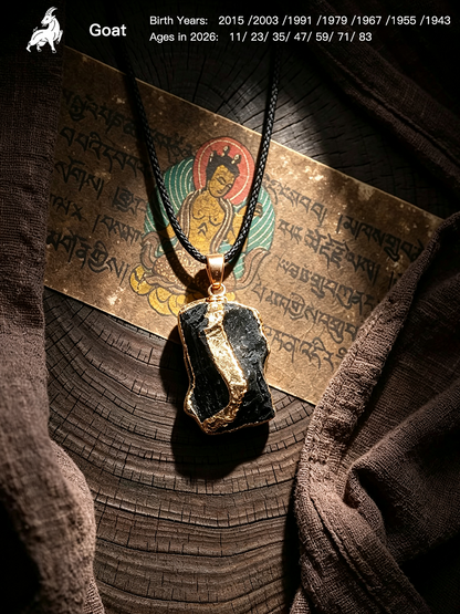 A black goat skull pendant with gold trim hangs on a black cord over a bronze-colored script card, set against a dark textured background with a wood grain surface and draped brown fabric.