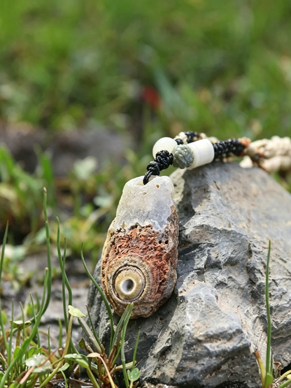 A beaded necklace with a natural shell pendant resting on a gray rock with green grass in the background.