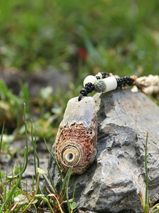 A beaded necklace with a natural shell pendant resting on a gray rock with green grass in the background.