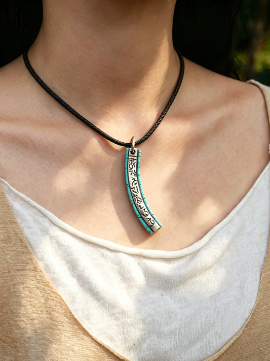 A close-up of a person wearing a black cord necklace with a curved turquoise and silver pendant featuring black engraved patterns.