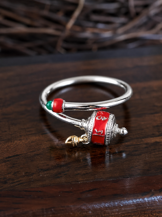 A silver-toned bangle bracelet with red and green enamel details and a dangling red-and-silver charm, displayed on a dark wooden surface.