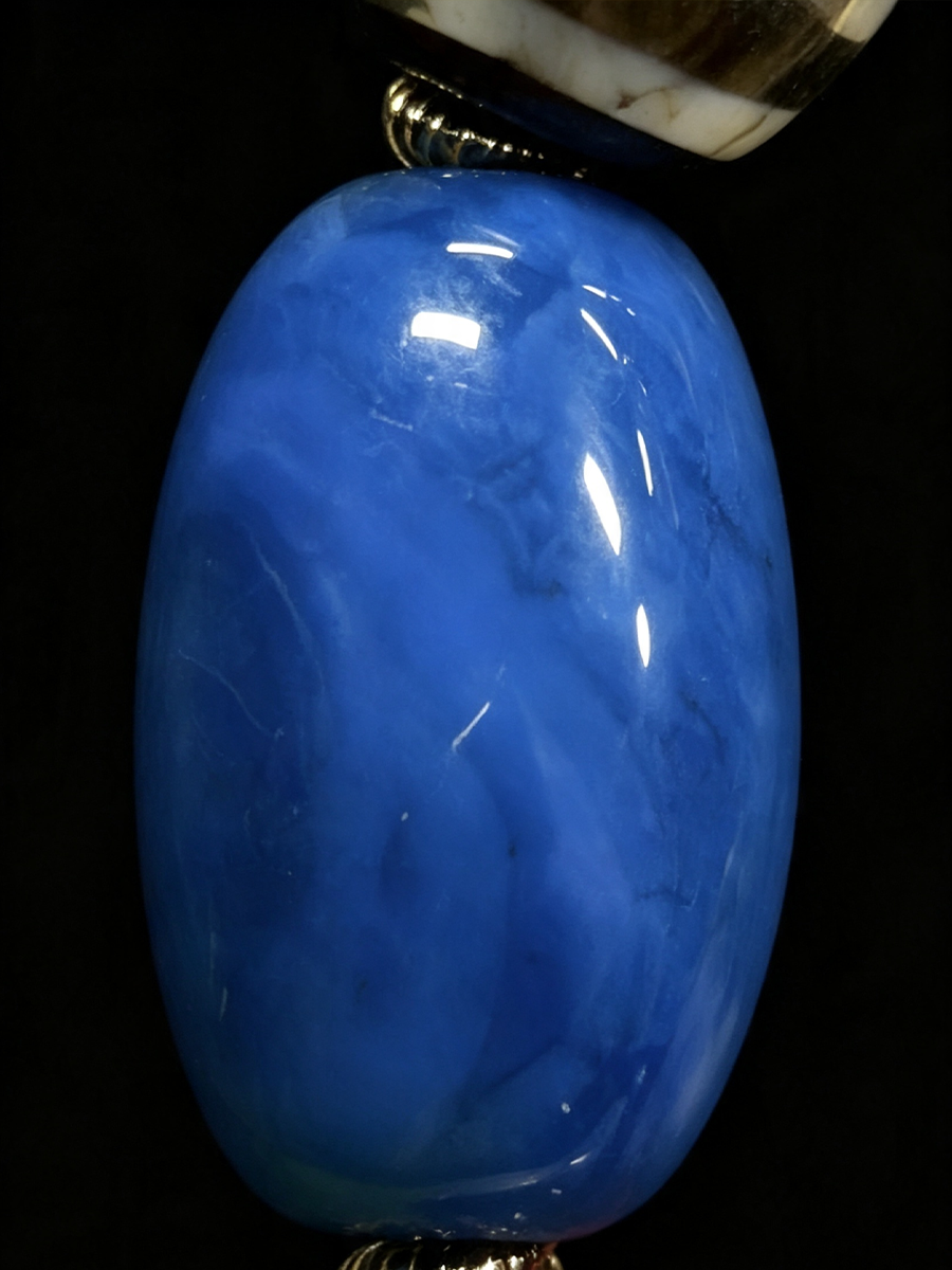 A glossy oval blue stone bead or pendant with natural marbling, shown against a solid black background.