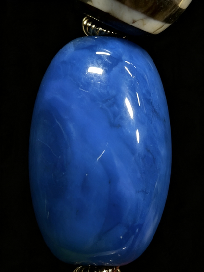 A glossy oval blue stone bead or pendant with natural marbling, shown against a solid black background.