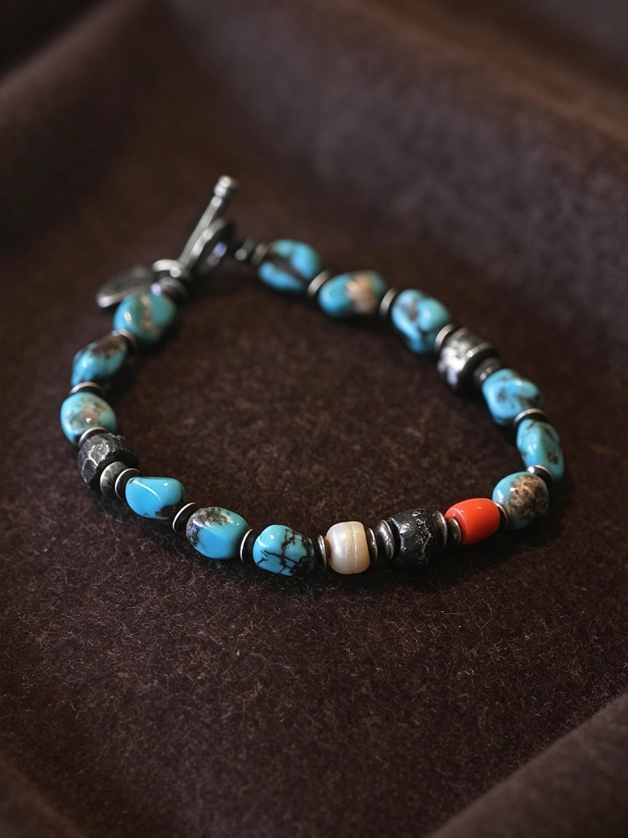 A beaded bracelet with turquoise blue, black, white, and orange beads, displayed on a dark brown velvet surface.