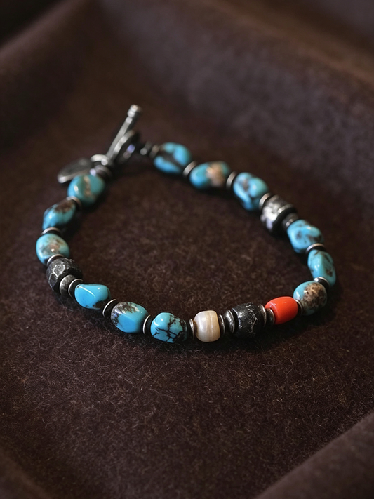 A beaded bracelet with turquoise blue, black, white, and orange beads, displayed on a dark brown velvet surface.