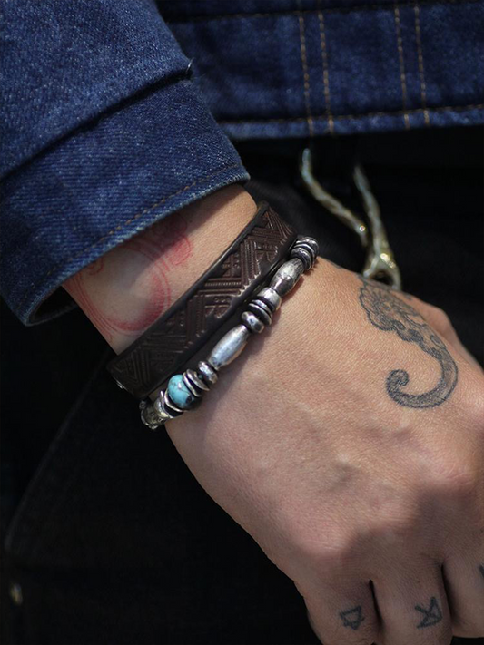Close-up of a wrist wearing a silver and brown bracelet with tattoos on the hand.