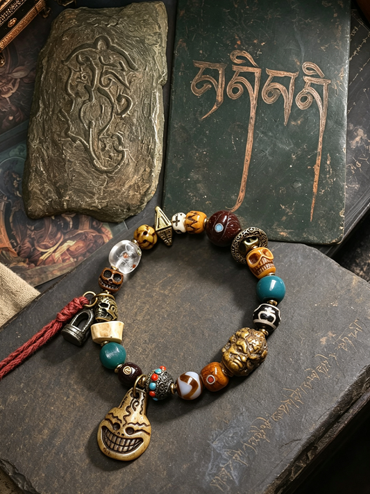 A beaded bracelet with a carved skull charm, turquoise beads, skull beads, and a red tassel, displayed on a dark stone surface next to Tibetan books.
