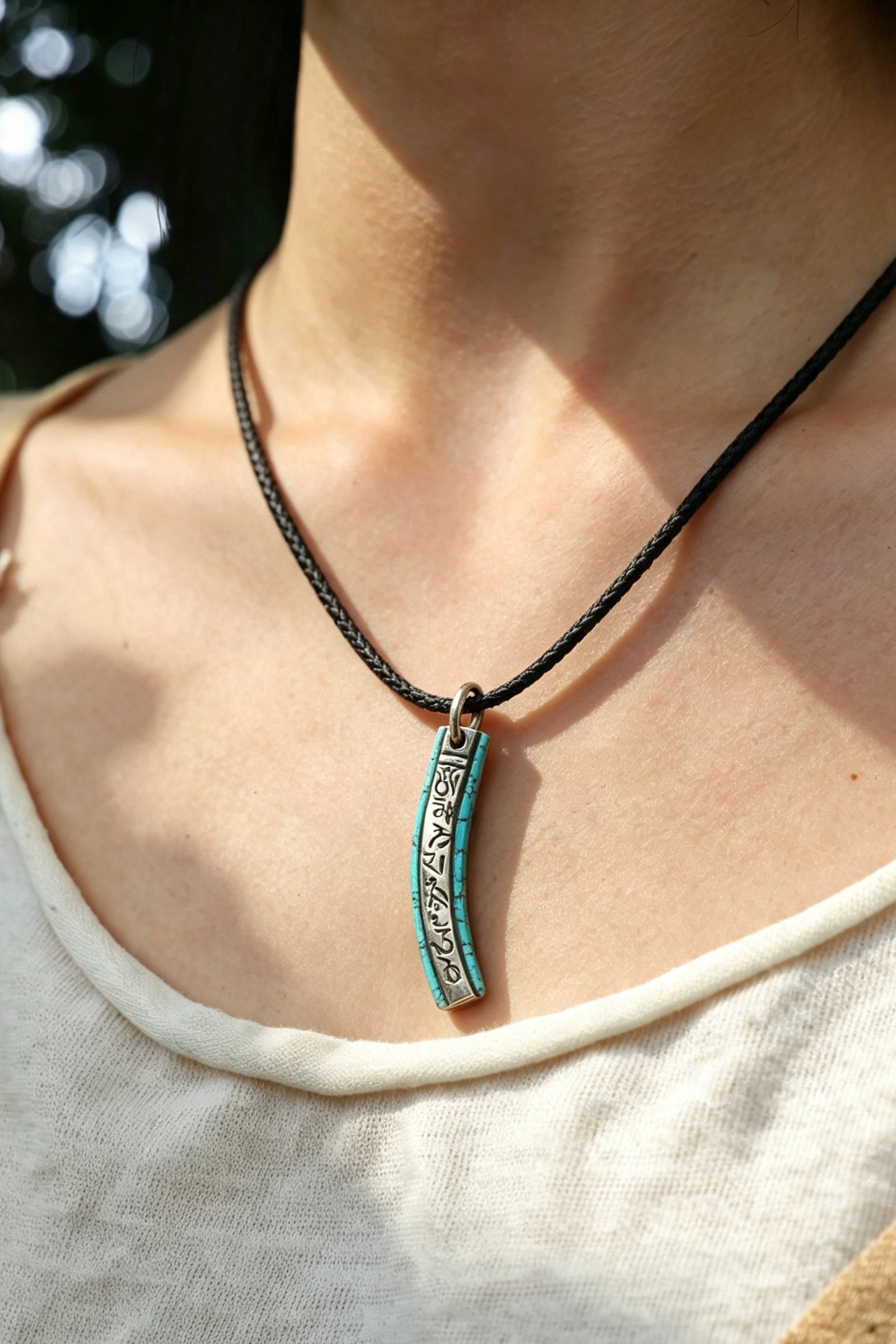 A close-up lifestyle shot of a person wearing a black braided cord necklace with a vertical turquoise and silver pendant.