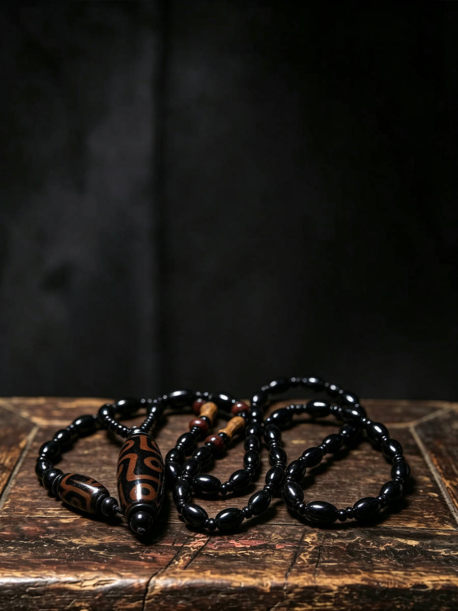A beaded necklace with glossy black beads and a central brown cylindrical bead featuring a carved black symbol, displayed on a rustic wooden surface against a dark background.