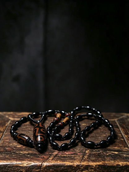 A beaded necklace with glossy black beads and a central brown cylindrical bead featuring a carved black symbol, displayed on a rustic wooden surface against a dark background.