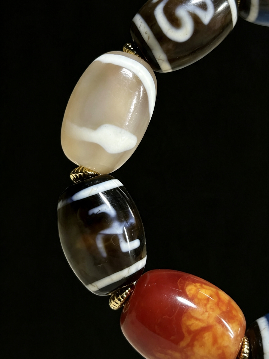 Close-up of a beaded jewelry strand featuring glossy, patterned glass beads in cream, black, white, and orange-red tones against a solid black background.
