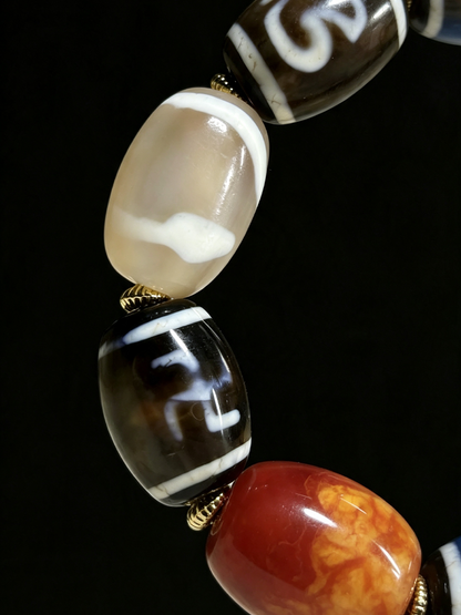 Close-up of a beaded jewelry strand featuring glossy, patterned glass beads in cream, black, white, and orange-red tones against a solid black background.