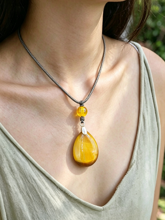 A close-up of a woman wearing a silver chain necklace with a large teardrop-shaped yellow amber pendant and a smaller round yellow accent bead.