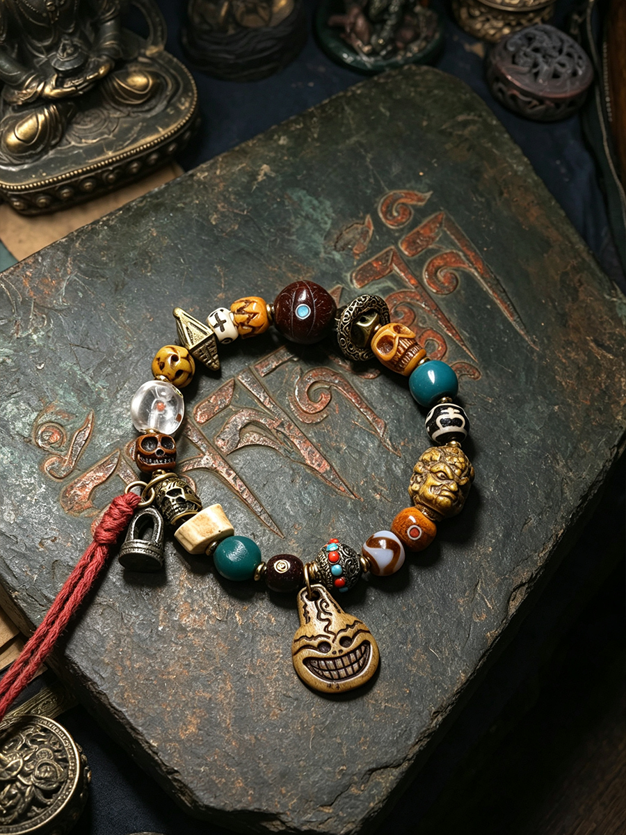 A beaded charm bracelet with a carved skull pendant, displayed on a dark textured stone surface. The bracelet features a mix of metallic bronze, turquoise, orange, white, and clear beads, along with small charms including a bell and a red cord tassel.