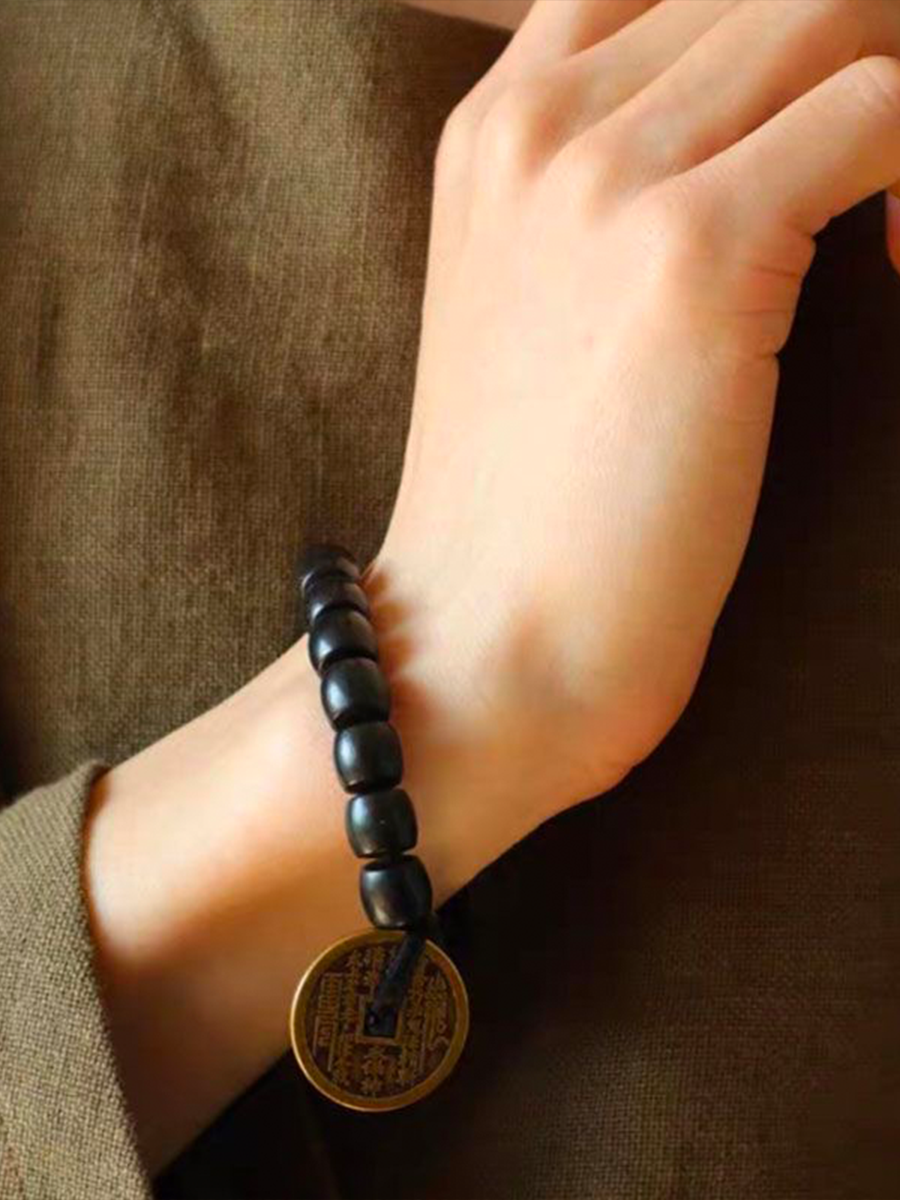 A person wearing an ebony bracelet adorned with a Taoist mountain spirit charm is displaying it in front of them.