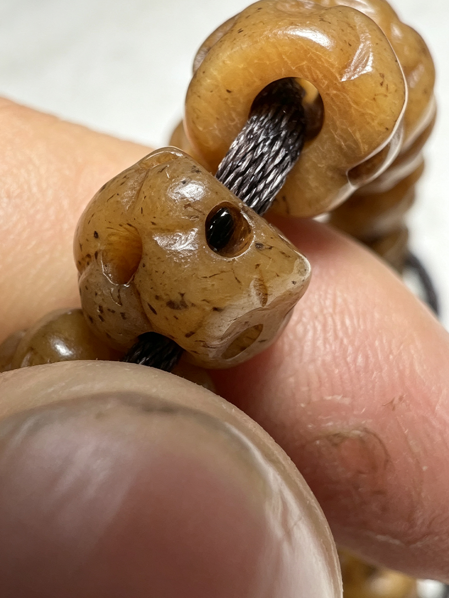 A close-up of a beaded necklace or bracelet with carved, polished brown beads threaded on a black cord, held between fingers.