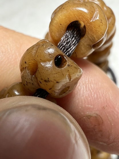 A close-up of a beaded necklace or bracelet with carved, polished brown beads threaded on a black cord, held between fingers.