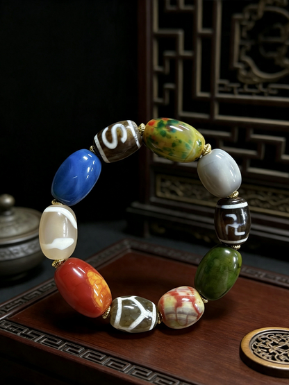 A beaded bracelet with nine distinct, polished stone beads in various colors including blue, green, red, orange, white, and brown, separated by small gold spacer rings, displayed on a dark wooden surface.