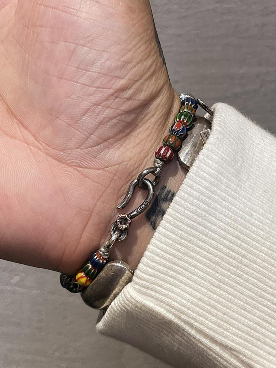 A close-up of a hand wearing a silver-toned bracelet with colorful glass beads and a silver horsebit charm, paired with a cream ribbed knit sleeve.