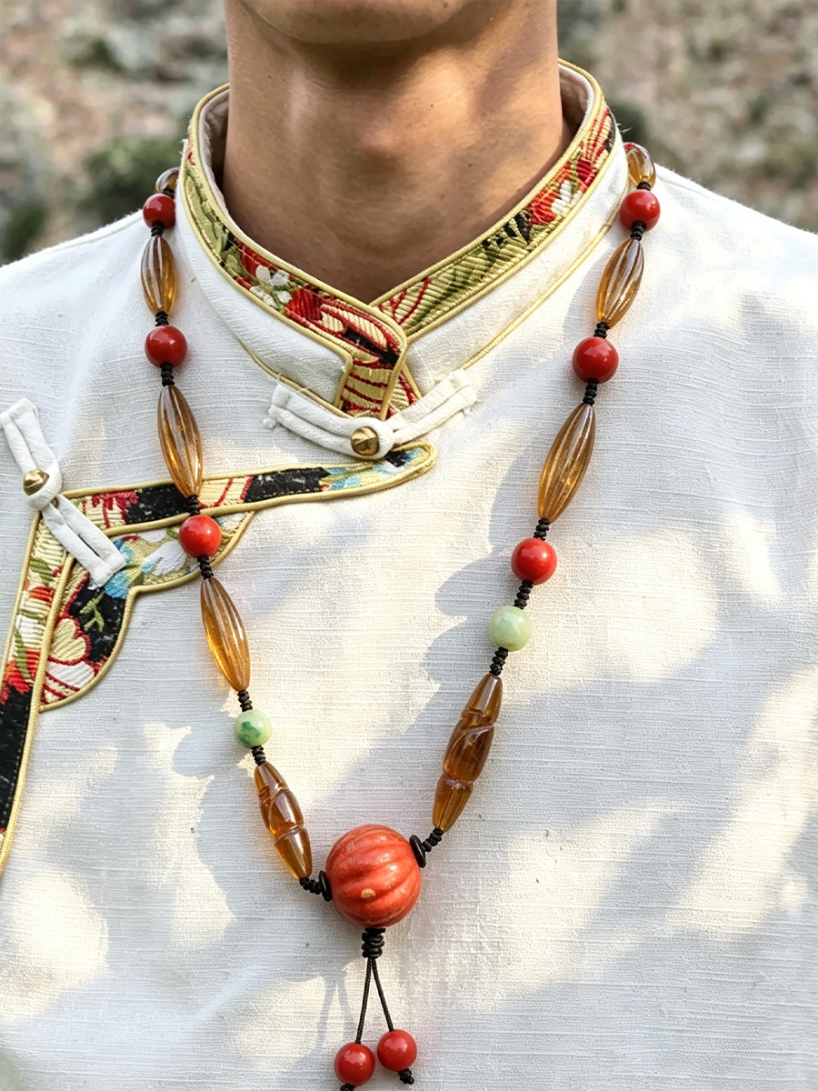 A close-up of a person wearing a traditional white embroidered Tibetan-style collar with a long beaded necklace featuring amber-brown elongated beads, red round beads, and small light green beads.