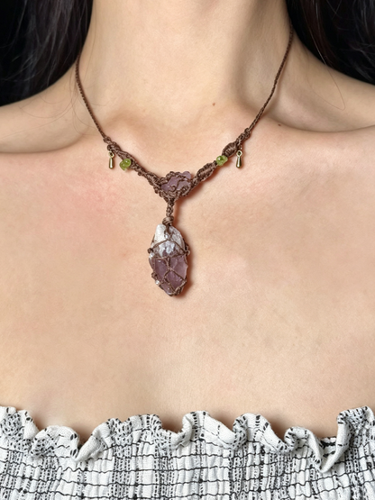 A close-up of a person's neck and upper chest wearing a handmade brown braided cord necklace with a large purple-brown and white textured pendant.