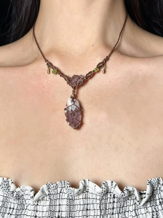 A close-up of a person's neck and upper chest wearing a handmade brown braided cord necklace with a large purple-brown and white textured pendant.