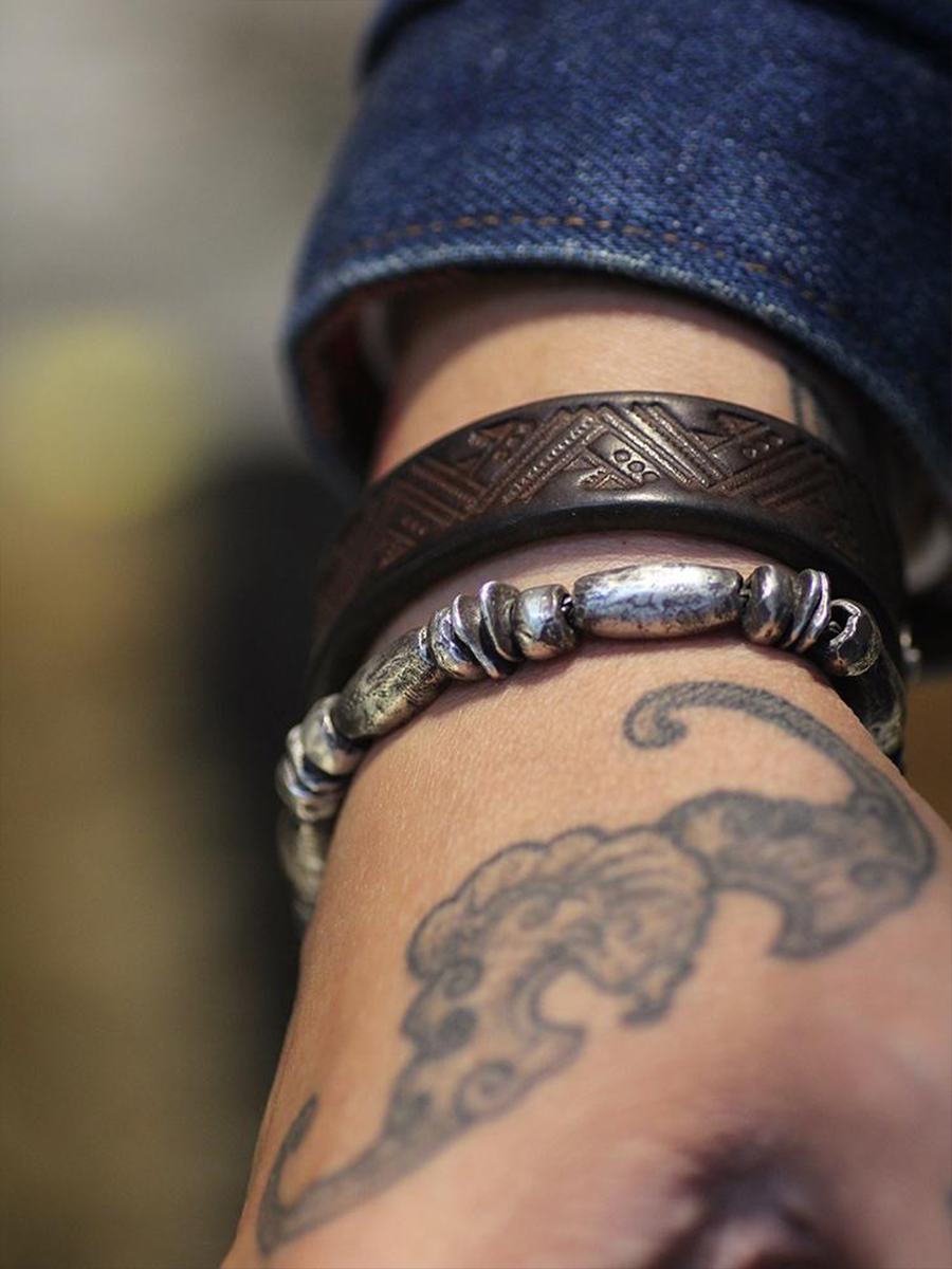 Close-up of a person's wrist wearing two bracelets with a tattoo on the skin.