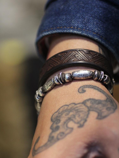 Close-up of a person's wrist wearing two bracelets with a tattoo on the skin.