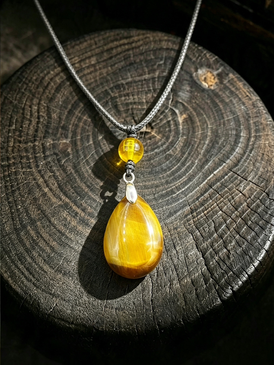 A silver chain necklace with a yellow teardrop-shaped stone pendant and a smaller yellow bead accent, displayed on a dark wood slice background.