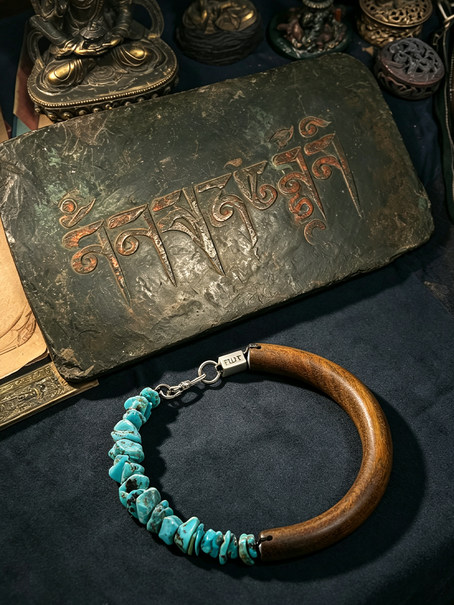 A wooden and turquoise stone bracelet displayed on a dark fabric surface, with an antique-style metal plaque featuring engraved script behind it.