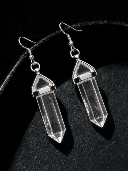 A pair of clear crystal point dangle earrings with silver-toned hooks and caps, displayed on a textured black surface.