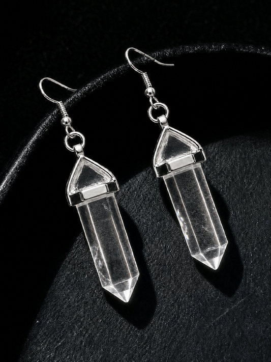 A pair of clear crystal point dangle earrings with silver-toned hooks and caps, displayed on a textured black surface.