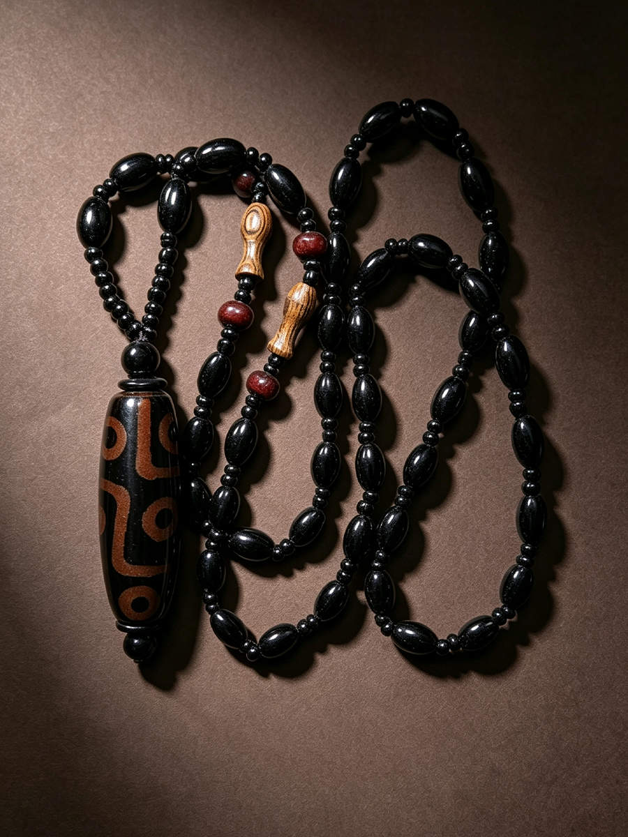 A black beaded necklace with a large patterned black and brown pendant, accented by small red beads and light wood details, arranged on a dark brown background.