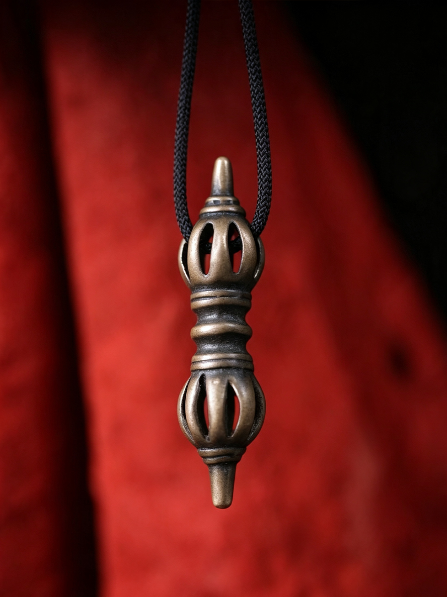 A metallic pendant with a carved, perforated design hangs from a black cord against a dark red textured background.