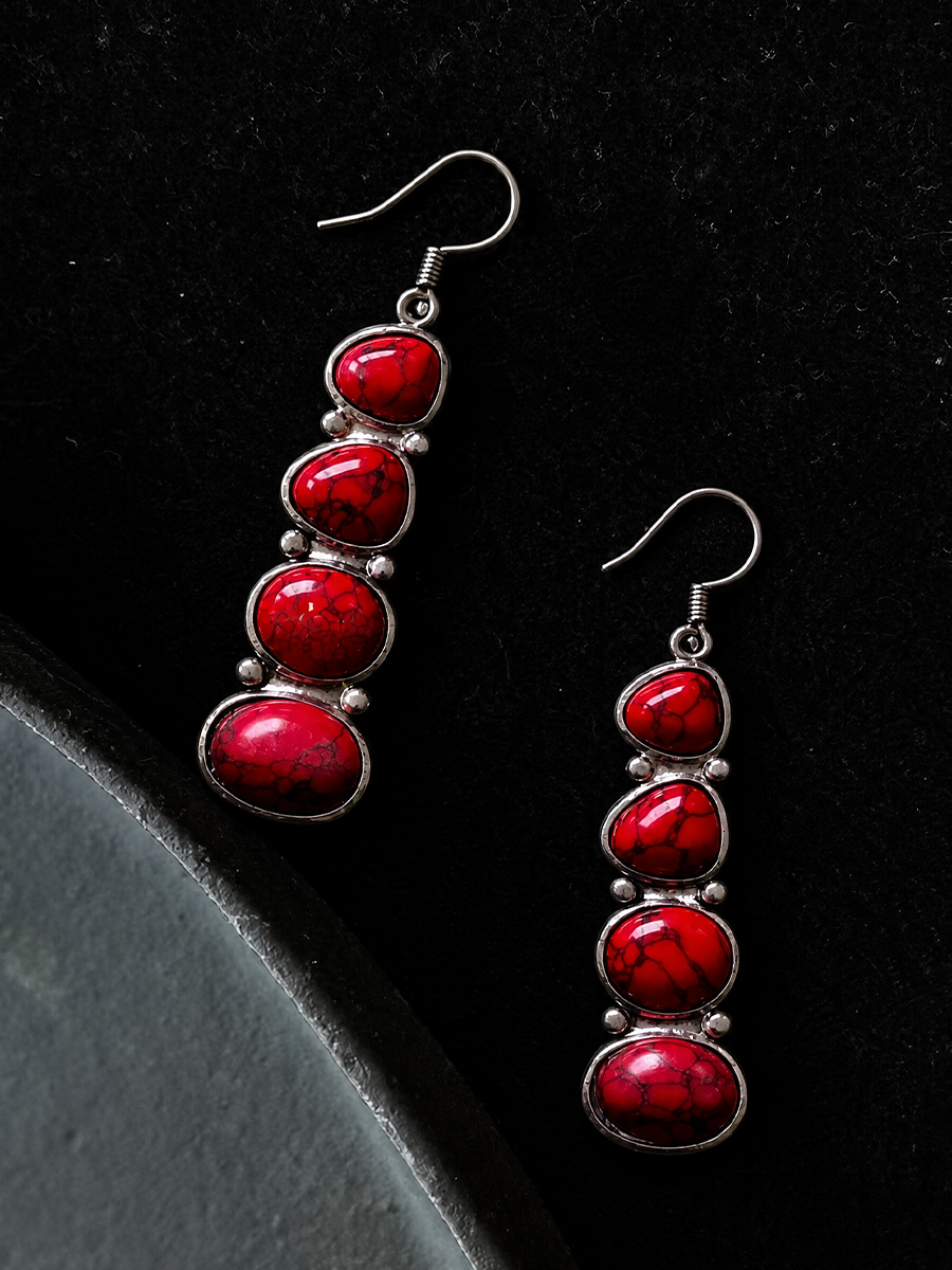 A pair of silver drop earrings with five stacked red marbled cabochon stones, displayed on a black textured background.