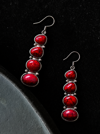 A pair of silver drop earrings with five stacked red marbled cabochon stones, displayed on a black textured background.