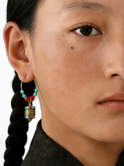 Close-up of a model wearing a gold hoop earring adorned with turquoise and red beads and a dangling cylindrical ornament.