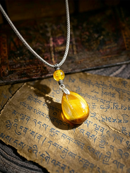 A silver chain necklace with a teardrop-shaped yellow amber pendant and a small round yellow bead, displayed on an aged paper with Tibetan script.