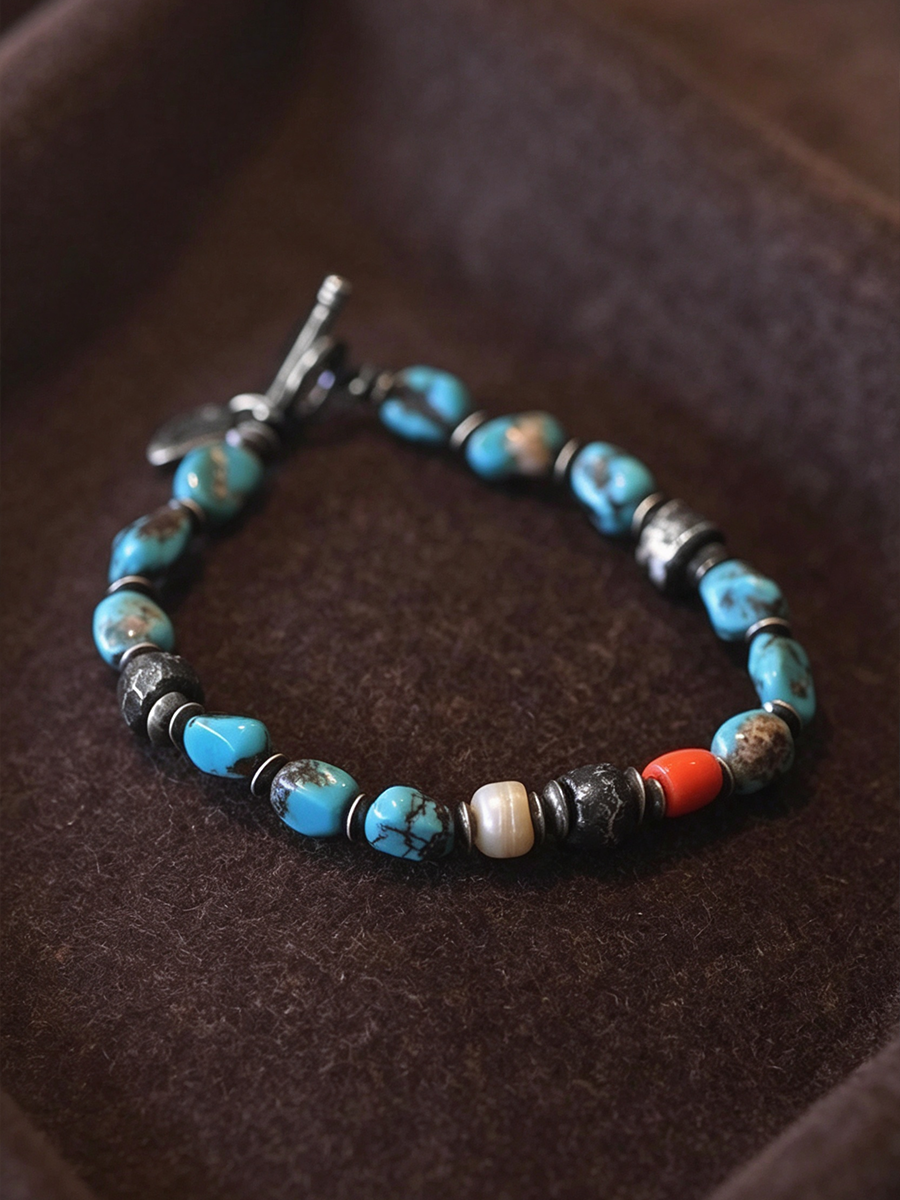 A beaded bracelet with turquoise blue, black, white, and red beads, displayed on a dark brown velvet surface.