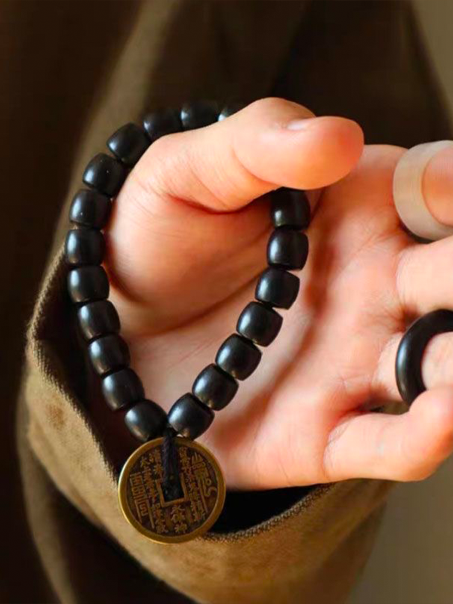 A person wearing an ebony bracelet adorned with a Taoist mountain spirit charm is displaying it in front of them.