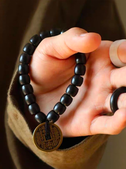 A person wearing an ebony bracelet adorned with a Taoist mountain spirit charm is displaying it in front of them.